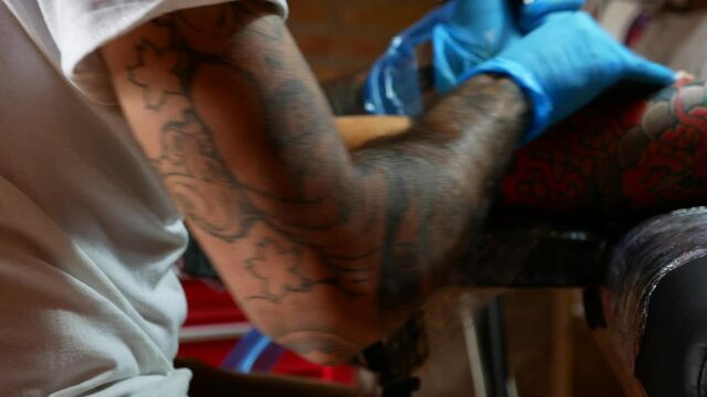 Panning scene of a tattoo artist working with a client in his studio.