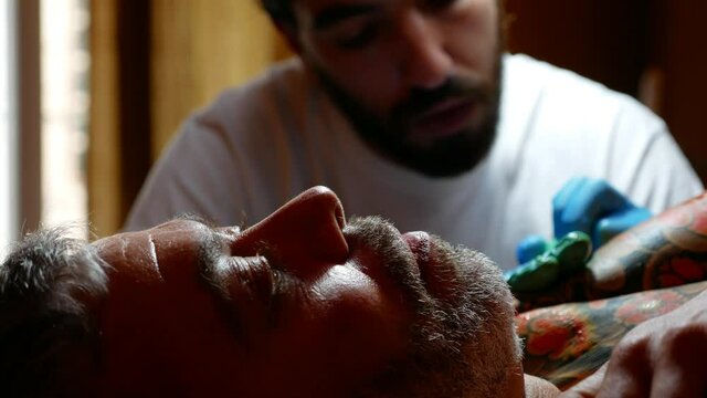 Front view of tattoo artist working with a customer in his studio.