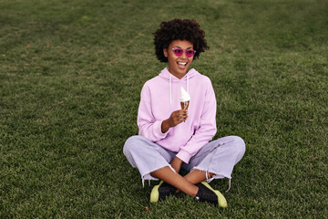 Attractive young brunette dark-skinned woman in stylish denim pants, purple hoodie and pink...