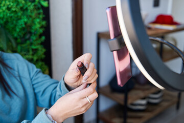 unrecognizable woman showing her lipstick in front of a tripod with circular light and her cell phone. female influencer blogger live in front of her smartphone. social media concept