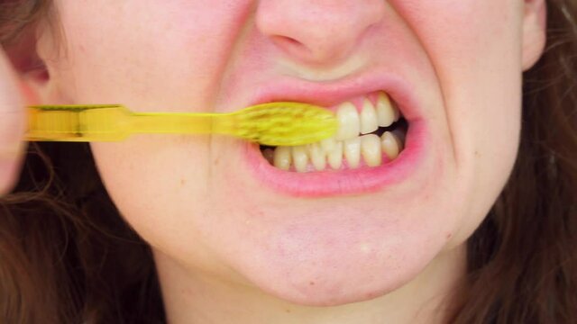 Young adult Caucasian woman brushes her teeth with a smile. Close-up of a face. Lips and oral hygiene. Care for clogs and gums. Dentist and check-up. We clean it correctly with a toothbrush.