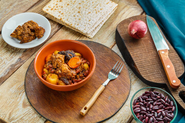 Jewish dish chelnt with meat on the table in a plate on a stand next to the ingredients and matzo.