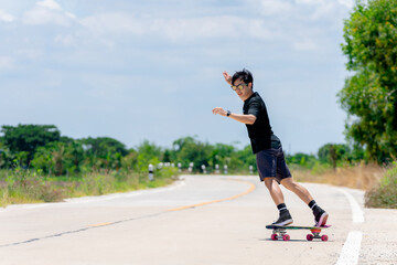 A young Asian man in a black shirt and pants is playing figure skating on a rural road. in the sun on a bright day, Play surf skate.