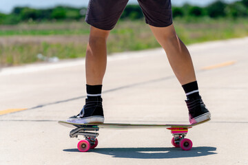 Fototapeta na wymiar Close Up A young Asian man's legs are skateboarding on a country road on a sunny and clear day., Play surf skate.
