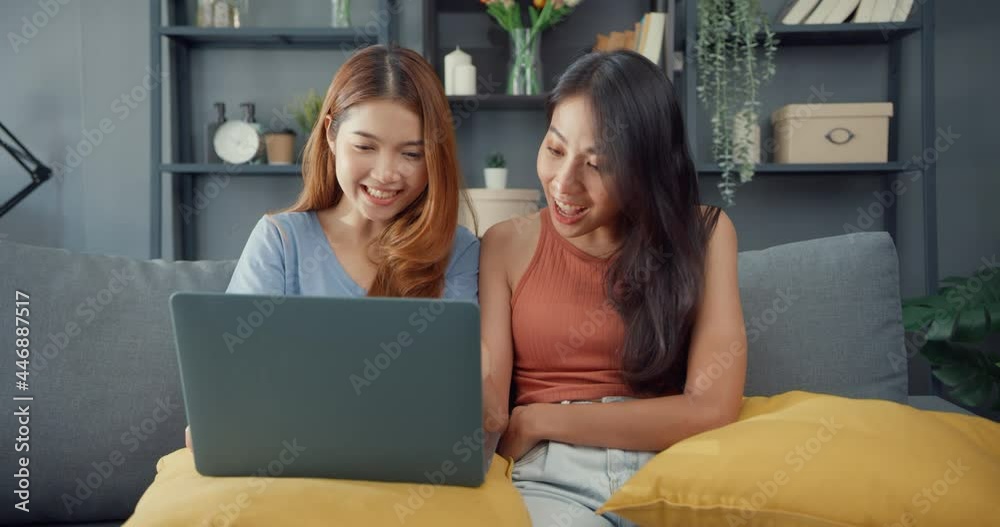 Wall mural two asia lesbian women site on couch together looking at laptop screen in living room at home togeth