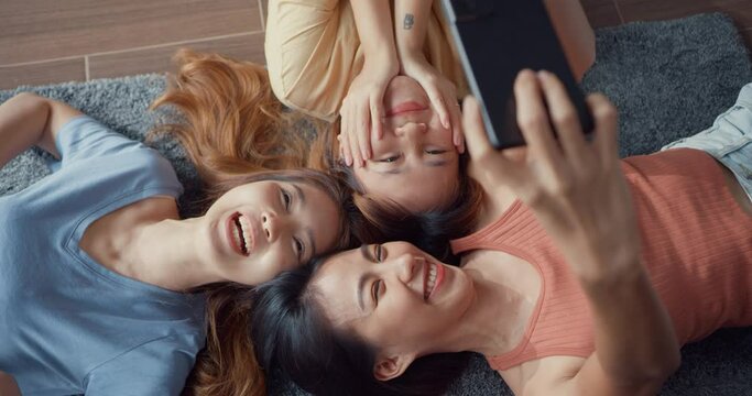 Above view close up group of Asia ladies with happiness enjoy moment hold smartphone smiling take memories picture lying on carpet in floor living room at home. Lifestyle activity quarantine concept.