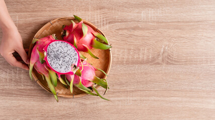 Dragon fruit or pitaya in a basket holding by woman hand on woden background, Tropical fruit, Table top view