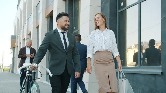 Slow motion of businessman and businesswoman colleagues walking in city street and holding bike. Urban transport and healthy lifestyle concept.