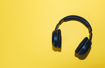 Black wireless headphones isolated on a yellow background. 