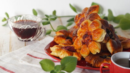 Beautiful yeast buns in the form of flowers for tea, in a red plate on a light background with mint sprigs.Food background.