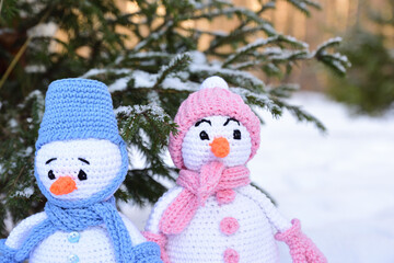 A close view of two knitted snowmen standing under a tree in the snow