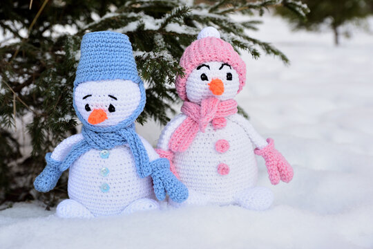 Two knitted snowmen stand in the snow under the tree
