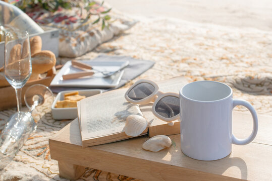 Image of beach picnic, mug of coffee, sunglasses and book on a tropical beach