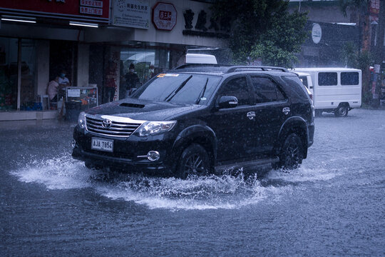 Metro Manila, Philippines - Aug 2020: A Toyota Fortuner wades through flash floods caused by heavy rains. Monsoon season or thunderclouds. Dramatic shot.