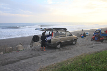 Fototapeta na wymiar Surfer next to ta car with waves in the background