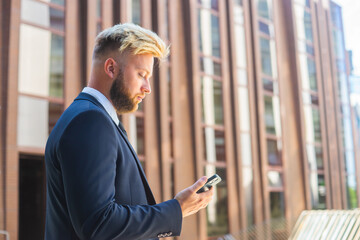 Confident businessman in front of modern office building. Financial investor is using smartphone outdoor. Banking and business.