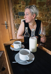 bottles of milk and coffee next to white mugs, in the background a blonde woman having breakfast