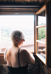 short-haired blonde woman in black nightgown leaning out of the window of a country hotel watching the sunrise.