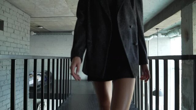 Female model walks along dark catwalk in her shoes at home and shows an outfit. The woman is blonde with her hair gathered in a bun. She is tall and slender. Loft style