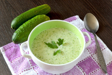 Cold soup of cucumbers in soup stands on a towel on a dark-colored table