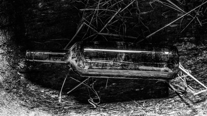 An old bottle of wine lies forgotten in a wooden manger, covered with hay and dust. Black and white photography.