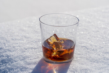Glass of whiskey with ice on a bed of snow and white background, close up