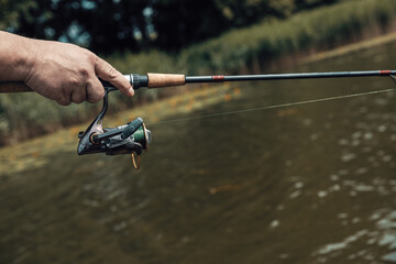 Fishing rod with a spinning reel in the hands of a fisherman in summer. Fishing background.