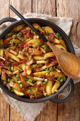 Fried potatoes with bacon and mushrooms close-up in a frying pan on the table. Vertical top view from above