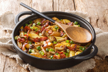 Freshly fried potato wedges with green onions, mushrooms and bacon close-up in a pan on a wooden background. horizontal
