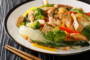 Stir fried of chicken, tofu, bell peppers, carrots, broccoli and bok choy close-up in a plate on the table. horizontal