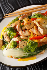 Stir fry vegetables, chicken and tofu close-up in a plate on the table. Vertical