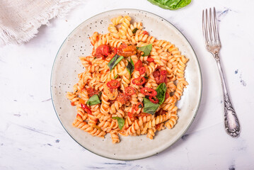 Fusilli pasta in tomato sauce with basil and hot pepper, serving on a plate, top view - vegetarian italian cuisine