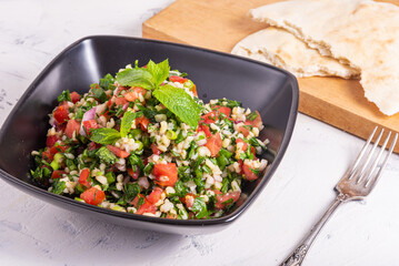 Traditional Lebanese salad tabbouleh decorated with mint leaves in black cup on the table with the pita bread in the background.
