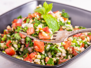 Traditional Lebanese Tabouleh salad garnished with mint leaves in a black cup and a fork with salad...