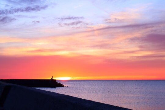 海に沈む夕陽が彩るオレンジ色と紫色の美しい夕焼け空 釣り人