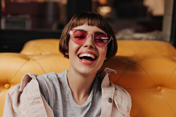 Optimistic woman with short hair laughing in cafe. Brunette girl in bright sunglasses and denim...