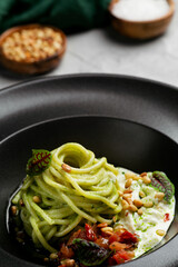 green pasta spaghetti with pesto sauce, tomatoes and basil. Pasta with spinach roasted vegetables and nuts