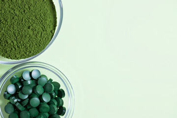 Chlorella powder and spirulina tablets on a green background. Organic food supplement. Copy space, top view, flat lay. - obrazy, fototapety, plakaty