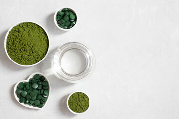 Chlorella green powder, spirulina pills and a glass of water on a white background. Superfood. Vegan organic supplements. Copy space, top view