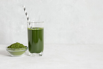 Chlorella green drink in a glass and powder in a bowl on a white concrete background. Detox drink and superfood concept. Natural supplement. Copy space.