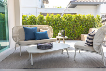 outdoor furniture rattan chairs, table and blue pillow by the home patio. Beautiful and cozy home outdoor space.