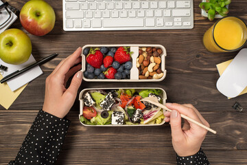 First person top view photo of hands eating healthy food salad berries nuts from two lunchboxes...