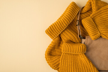 Top view photo of yellow knitted pullover and leather bag on isolated pastel beige background with empty space