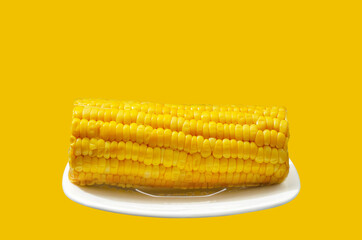 Boiled corn cob on a plate and a yellow background