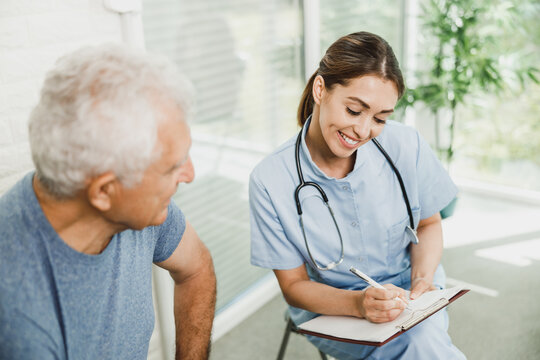 Caring Nurse Showing Medical Record To Senior Man At Medical Clinic