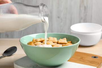 Pouring milk into bowl of tasty corn pads served for breakfast on table