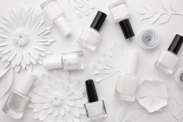 Bottles of white nail polish are aesthetically laid out on a white background with white paper flowers. - obrazy, fototapety, plakaty