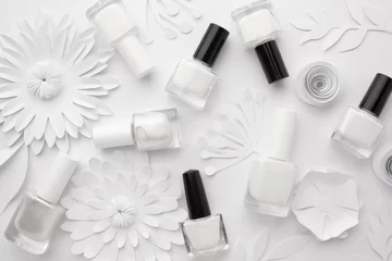  Bottles of white nail polish are aesthetically laid out on a white background with white paper flowers. © Alina Zavhorodnii