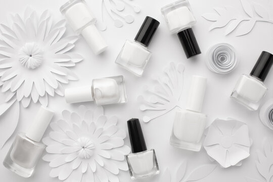 Bottles of white nail polish are aesthetically laid out on a white background with white paper flowers.