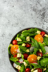 Delicious healthy salad of spinach leaves, tangerine and avocado slices, tomato and radish with seeds, salad in a plate close-up ,top view,copy space